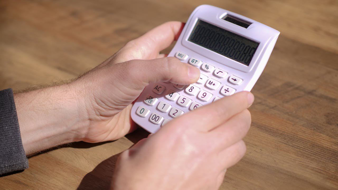 Hands using a pink calculator on a wooden table, emphasizing calculation and mathematics.